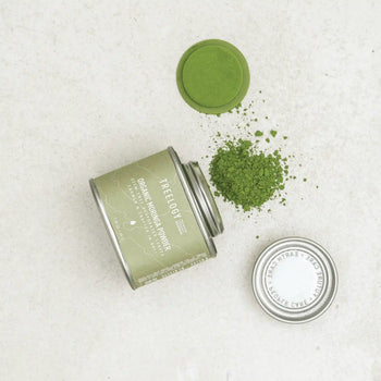 Open tin of Treelogy Moringa Powder with spilled vibrant green powder showing freshness and minimal eco-packaging.