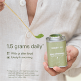 Moringa powder being scooped from a tin, with a guide recommending 0.5 tsp daily, preferably in the morning with meals.