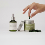 LANG:EN|Hand picking a capsule from a Treelogy organic moringa capsules container with a dropper bottle on a white background