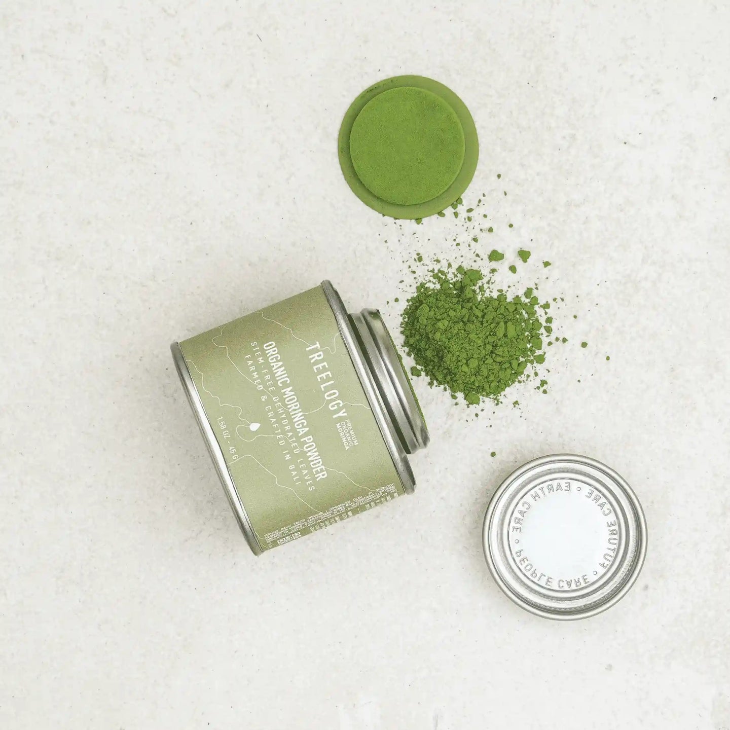 Open tin of Treelogy Moringa Powder with spilled vibrant green powder showing freshness and minimal eco-packaging.