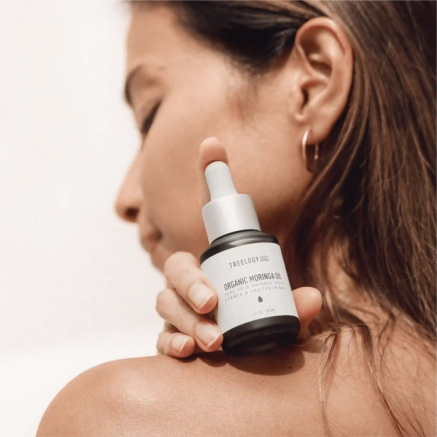 Seorang wanita mengaplikasikan Treelogy Organic Moringa Oil di bahunya, menampilkan perawatan kulit alami dengan minyak biji cold-pressed.