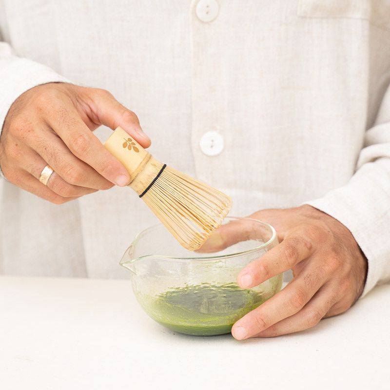 A hand mixing ingredients in a clear glass bowl next to the Treelogy Ritual Set, emphasizing the mindful self-care and natural wellness ritual experience.