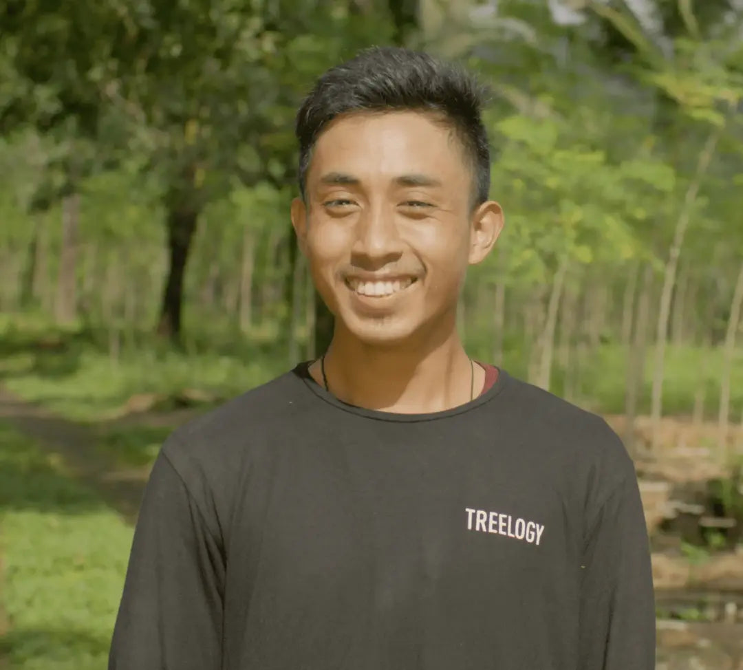 I Gede Suastika smiling outdoors with a natural background of trees and plants.