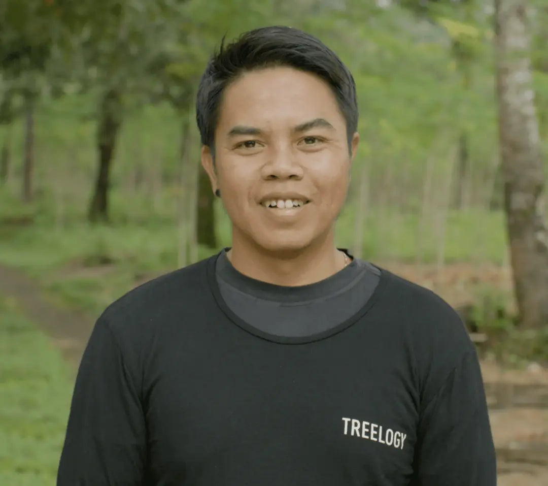 I Kadek Juniantara standing in a garden setting with plants and trees in the background.