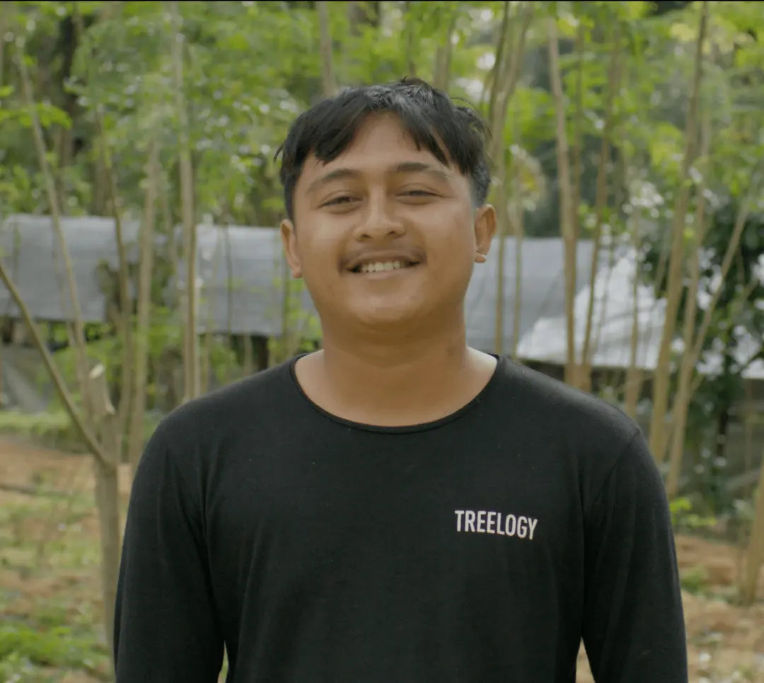 I Ketut De Juliana standing outdoors with trees and greenery in the background.
