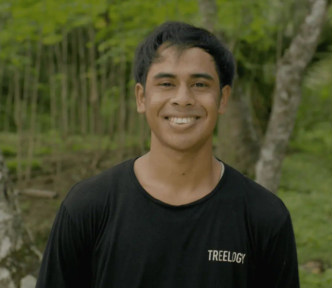 I Komang Darma smiling outdoors with greenery and a garden area in the background.
