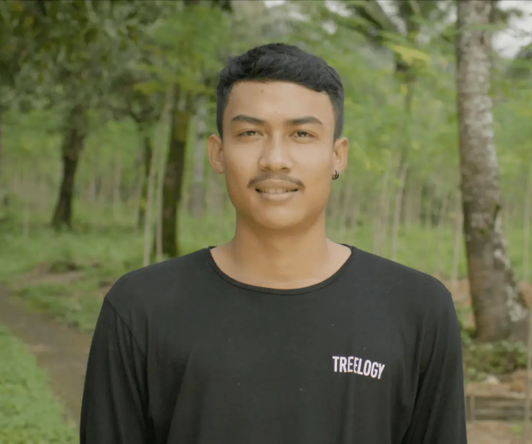 I Komang Mertayasa standing outside with a background of trees and natural greenery.