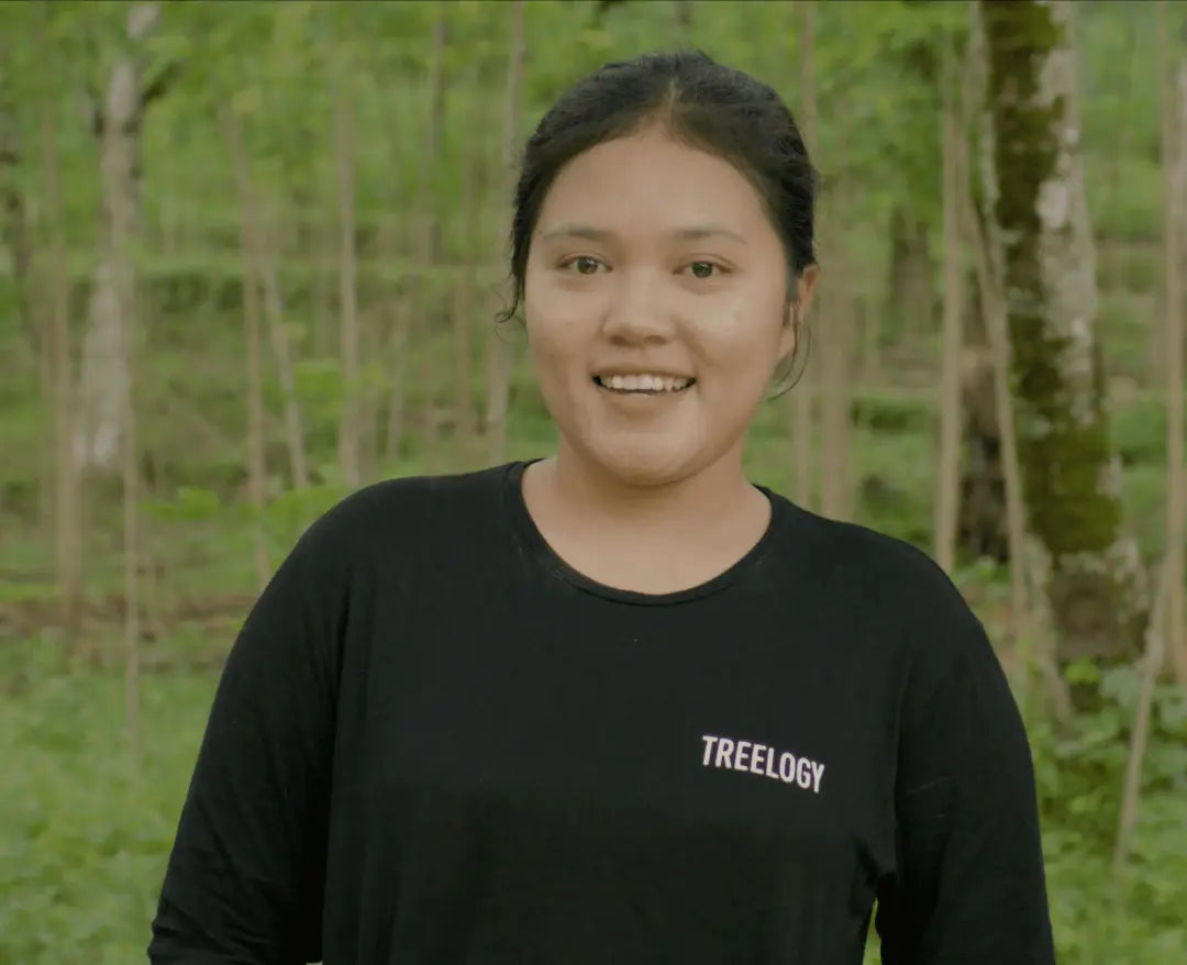 Novitasari Napitupulu smiling while standing outdoors in a garden area with trees in the background.